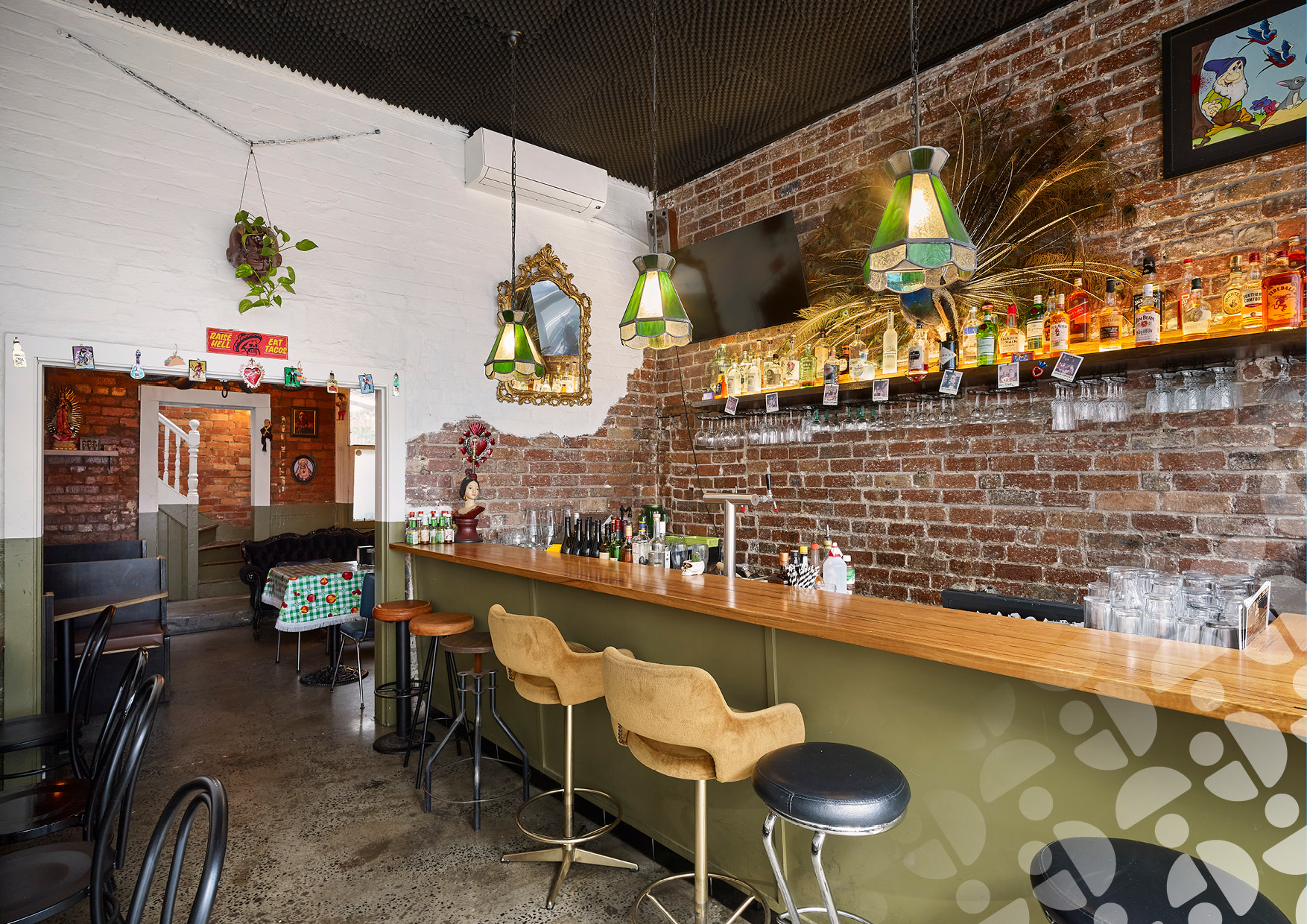 Bar interior with brick walls, hanging green stained-glass lamps, and a row of liquor bottles behind a wooden counter.