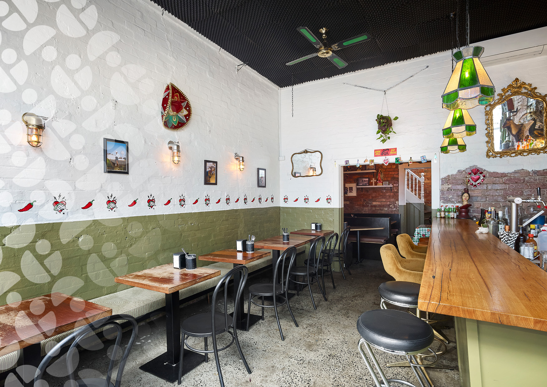 Long wooden bar with black stools along a white brick wall decorated with chili-pepper border and framed pictures.